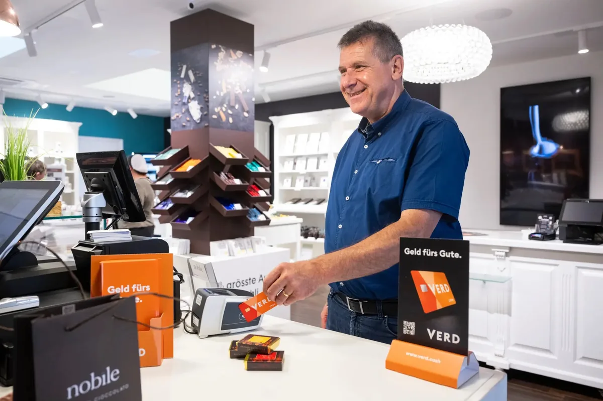 Ein Herr bezahlt mit einer orangen Karte an einem Kartenterminal.